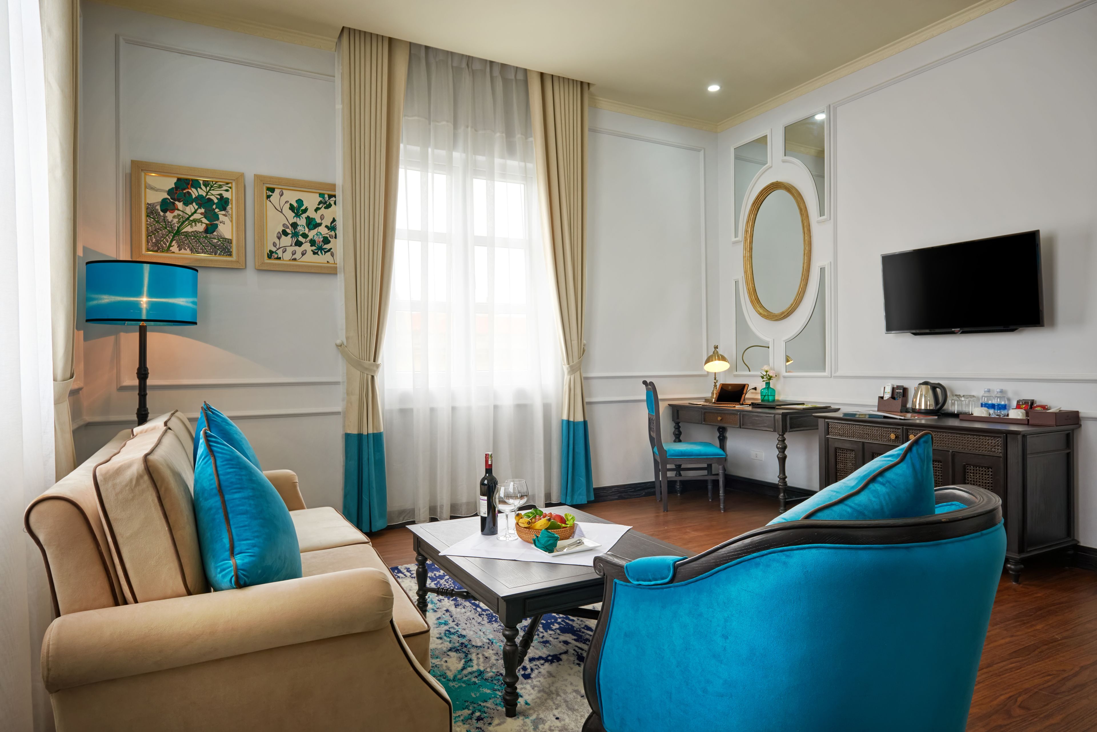 A hotel room with a sofa, a chair, a desk, a television, and a window with curtains.