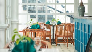 A dining area with wooden chairs and tables, large windows with a view of bicycles, and a blue railing.