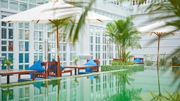 A pool area with lounge chairs and umbrellas, surrounded by glass windows and palm trees.