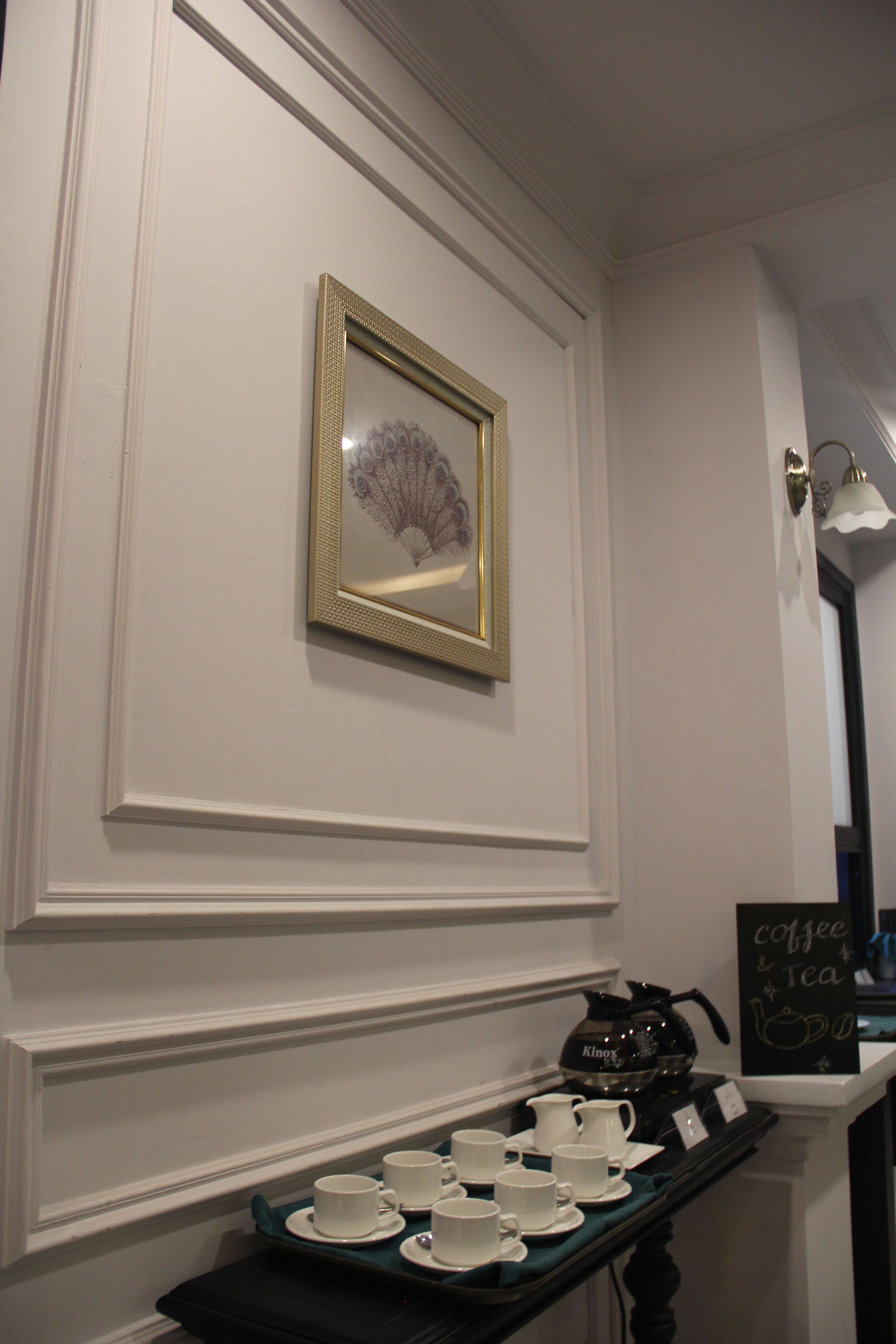 A wall with a framed picture, a tray with cups and a kettle, and a sign that says "coffee & tea".