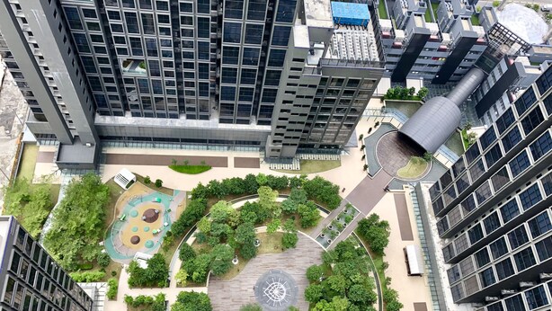 Une vue aérienne d’un quartier urbain moderne, avec de hauts immeubles, une place circulaire centrale entourée de verdure et une structure cylindrique imposante.