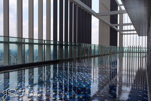 Piscina interior moderna con barandilla de vidrio, ventanas amplias y vista a un paisaje urbano.