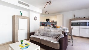 Un saló modern amb un sofà, una taula de centre i una zona de menjador amb taula i cadires. Es veu una cuina al fons amb electrodomèstics i una taula de dinar preparada.