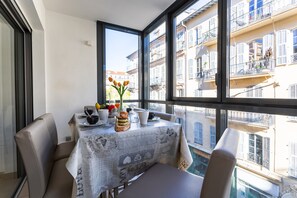 En matplats med ett bord dukat för två personer, en vas med blommor och utsikt över en bostadsbyggnad genom stora fönster.