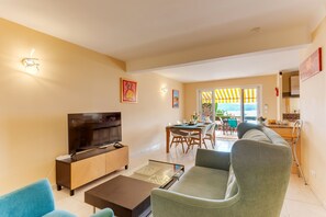 A living room with a flat-screen TV, a wooden cabinet, a sofa, and a dining area with a table and chairs. - LA MALMAISON AP1064 by RIVIERA HOLIDAY HOMES (Villefranche-sur-Mer)