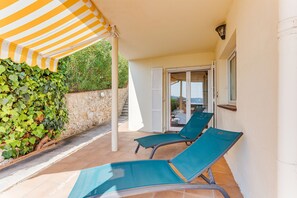 A covered outdoor area with two lounge chairs, a stone wall, and a view of the sea through a glass door. - LA MALMAISON AP1064 by RIVIERA HOLIDAY HOMES (Villefranche-sur-Mer)