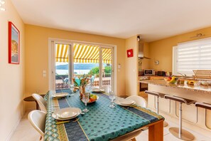 A dining area with a table set for four, a kitchen with modern appliances, and a view of a body of water through large windows. - LA MALMAISON AP1064 by RIVIERA HOLIDAY HOMES (Villefranche-sur-Mer)