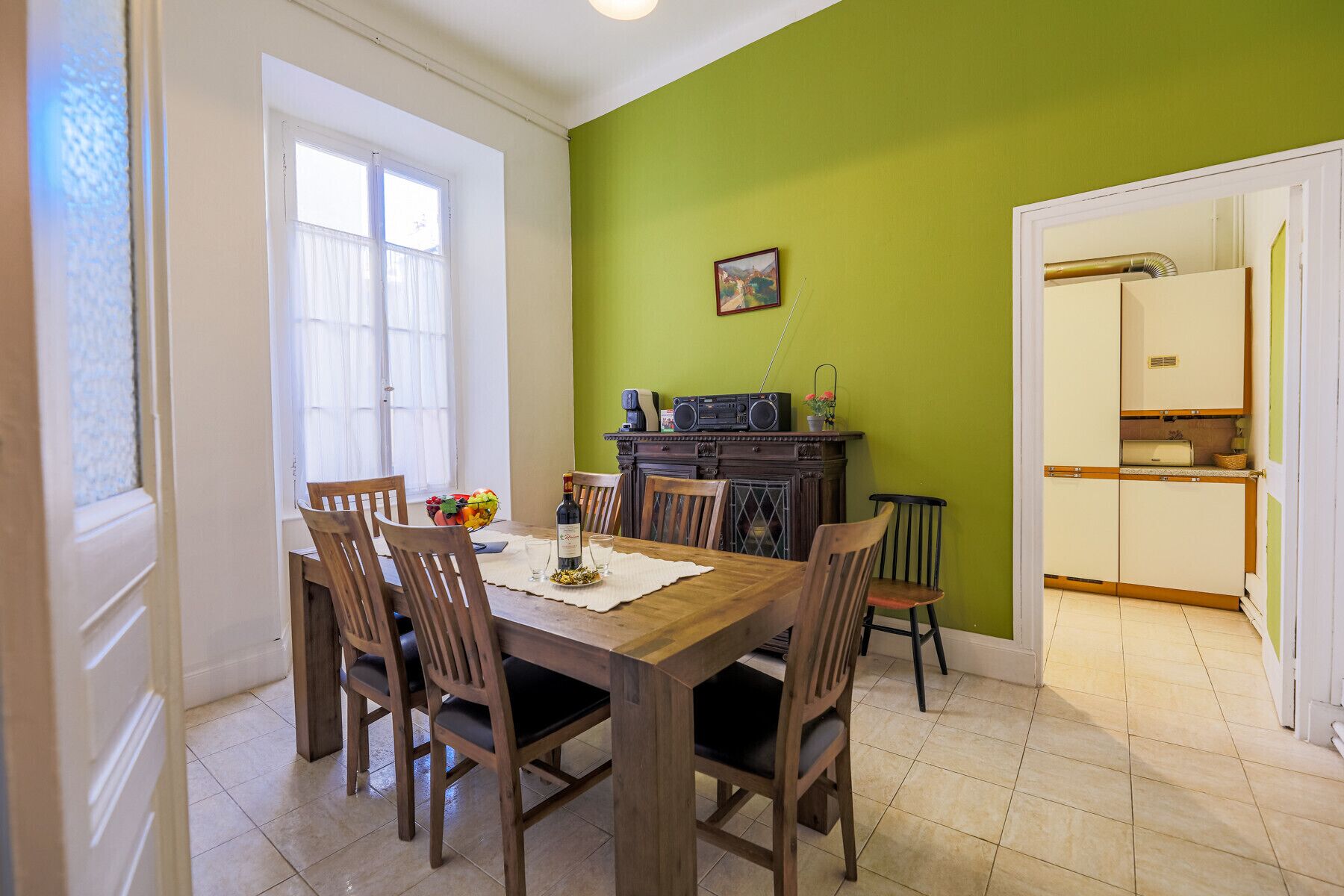 Een eetruimte met een houten tafel, stoelen, een radio en een schaal fruit.