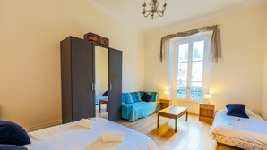 Habitación de hotel con dos camas, un sofá, una mesita, un armario y una ventana con cortinas.