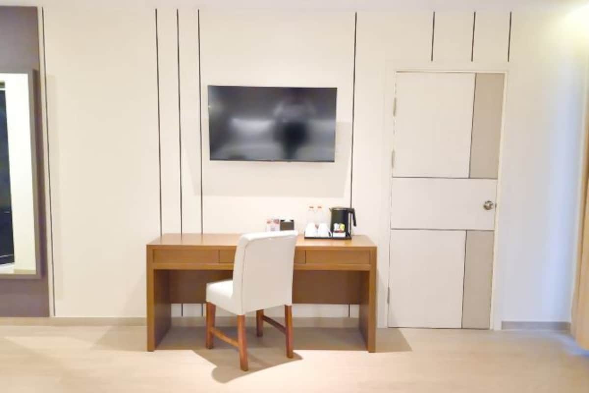 Una habitación con un escritorio de madera, una silla blanca, un televisor montado en la pared y un armario.