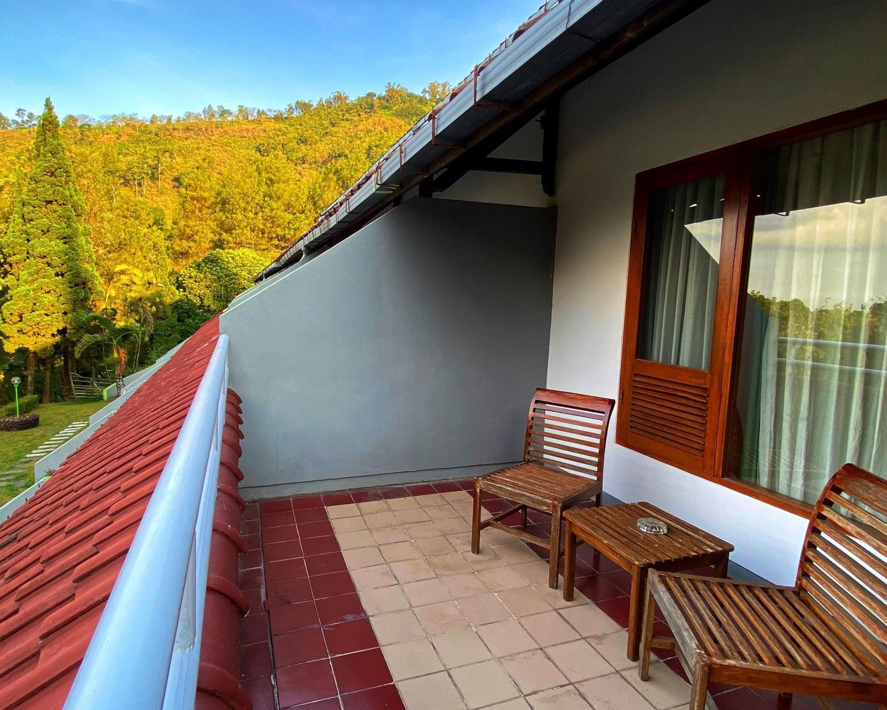 Un balcon doté d’un toit rouge, de deux chaises en bois, d’une petite table et d’une fenêtre avec des rideaux.