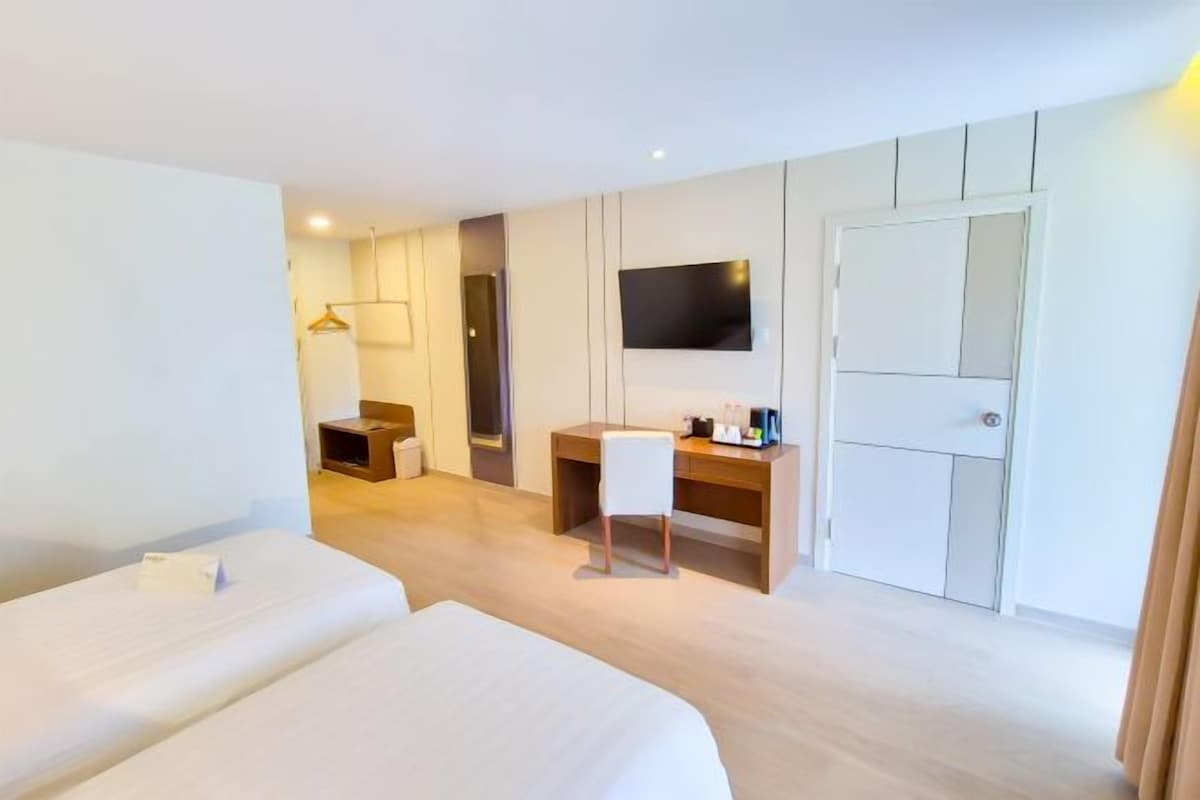 Habitación de hotel con dos camas, un escritorio, un televisor montado en la pared y un armario.
