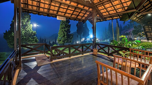 Una terraza de madera con barandilla, un banco y vistas a un paisaje montañoso al anochecer.