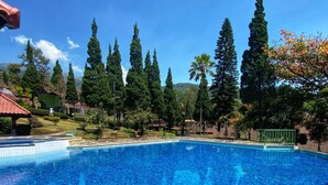 Una piscina azul cristalina rodeada de altos árboles y un pequeño pabellón.