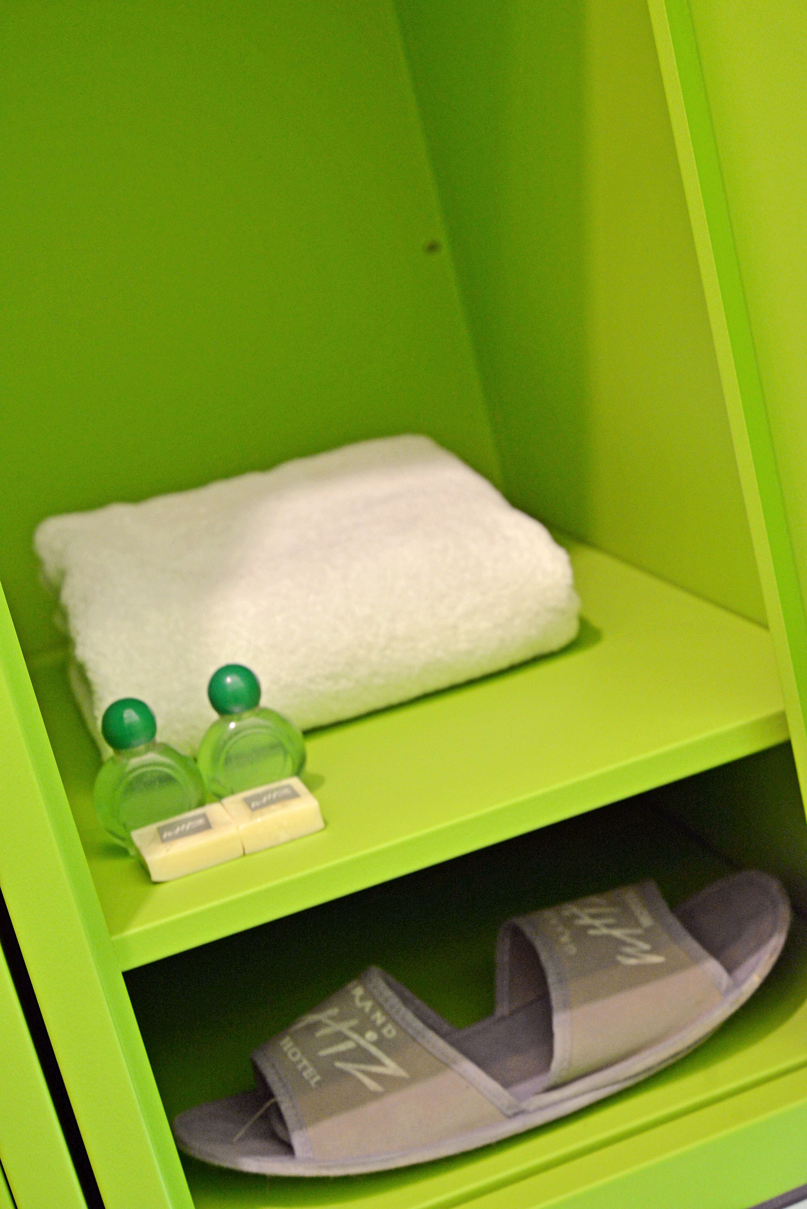 A green shelf with a white towel, two green bottles, and a pair of gray slippers.