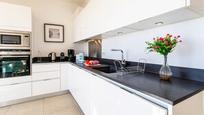 A modern kitchen with white cabinets, a black countertop, a stainless steel sink, a microwave, and a vase with flowers. - VILLA HENRIETTA AP4070 by RIVIERA HOLIDAY HOMES (Villefranche-sur-Mer)