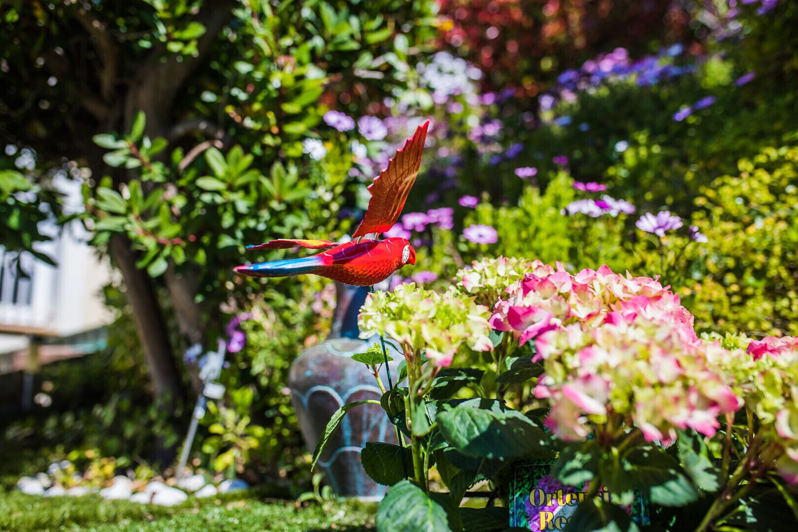 Ein Garten mit Vogel-Skulptur, Blumen und einer Zier-Vase.