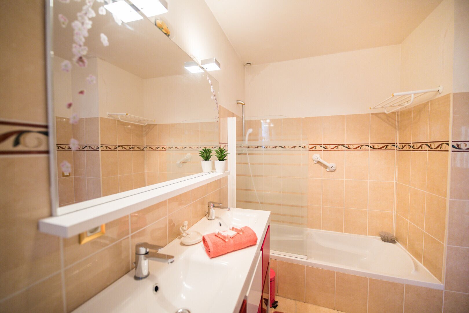 A bathroom with a sink, mirror, and bathtub. There are two potted plants on the vanity.