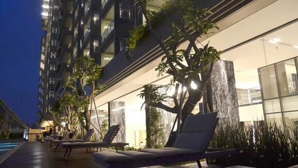 A modern hotel with a poolside area featuring lounge chairs and a water feature.