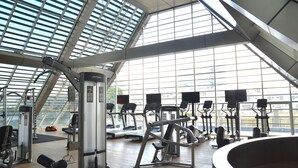 A gym with various exercise equipment, large windows, and a high ceiling.