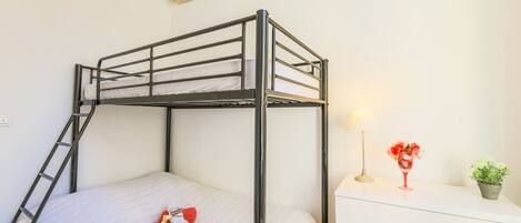 A bunk bed with a ladder, a bedside table with a lamp, and a small plant.