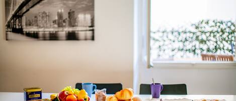 Une table de petit-déjeuner avec un panier de fruits, des viennoiseries et une boîte de thé Twinings Breakfast.