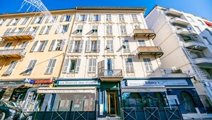 A multi-story building with a classic European architectural style, featuring a central entrance with a green awning, multiple balconies, and various commercial establishments on the ground floor. - CARRE D' OR TERRACE AP4015 by RIVIERA HOLIDAY HOME (Niza)