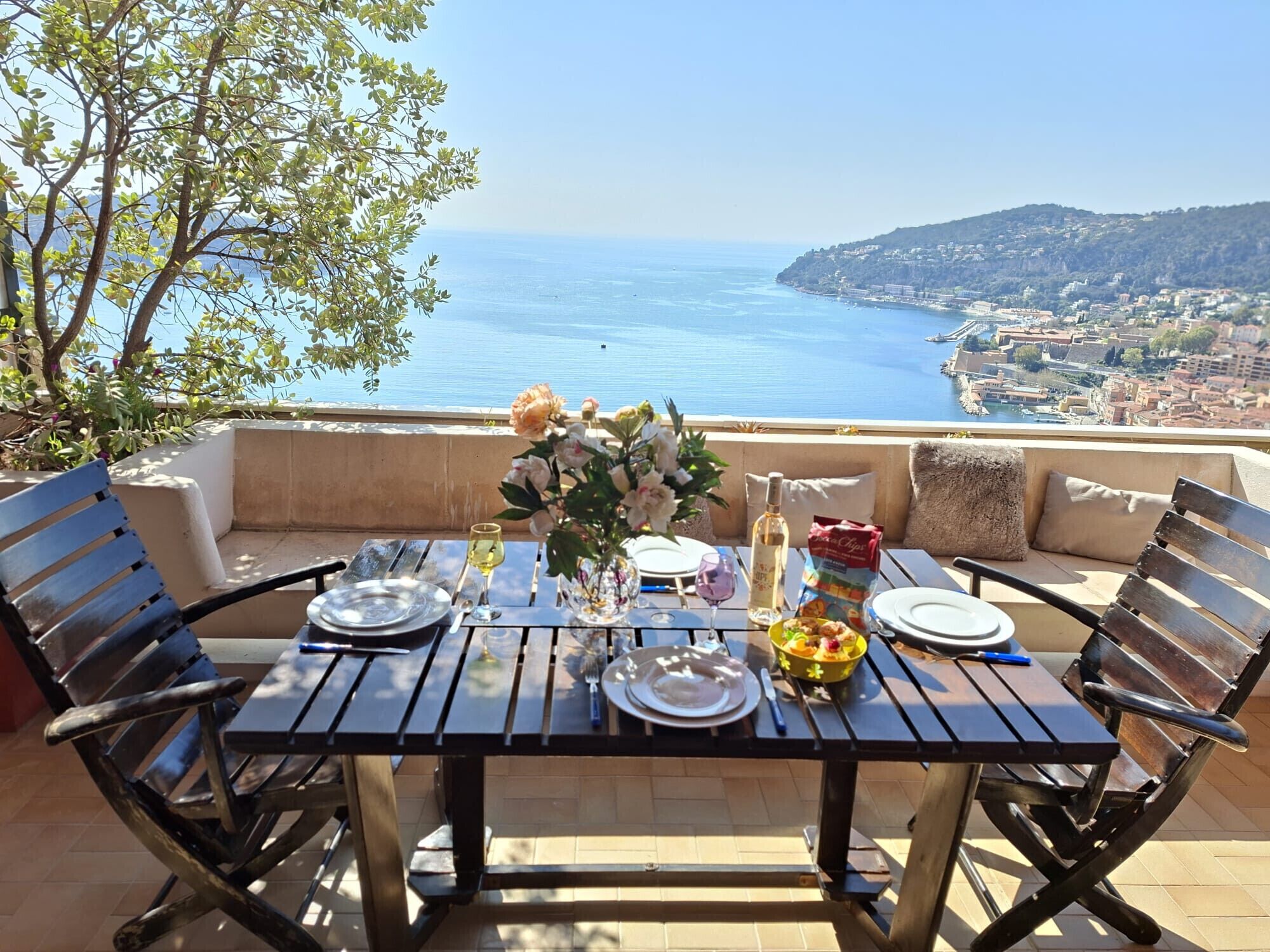 Une table dressée pour deux personnes, avec vue sur la mer et une ville en arrière-plan.