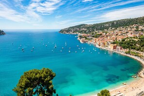 Una località costiera con un porto turistico pieno di barche, una spiaggia sabbiosa e una zona urbana densa con architetture storiche.