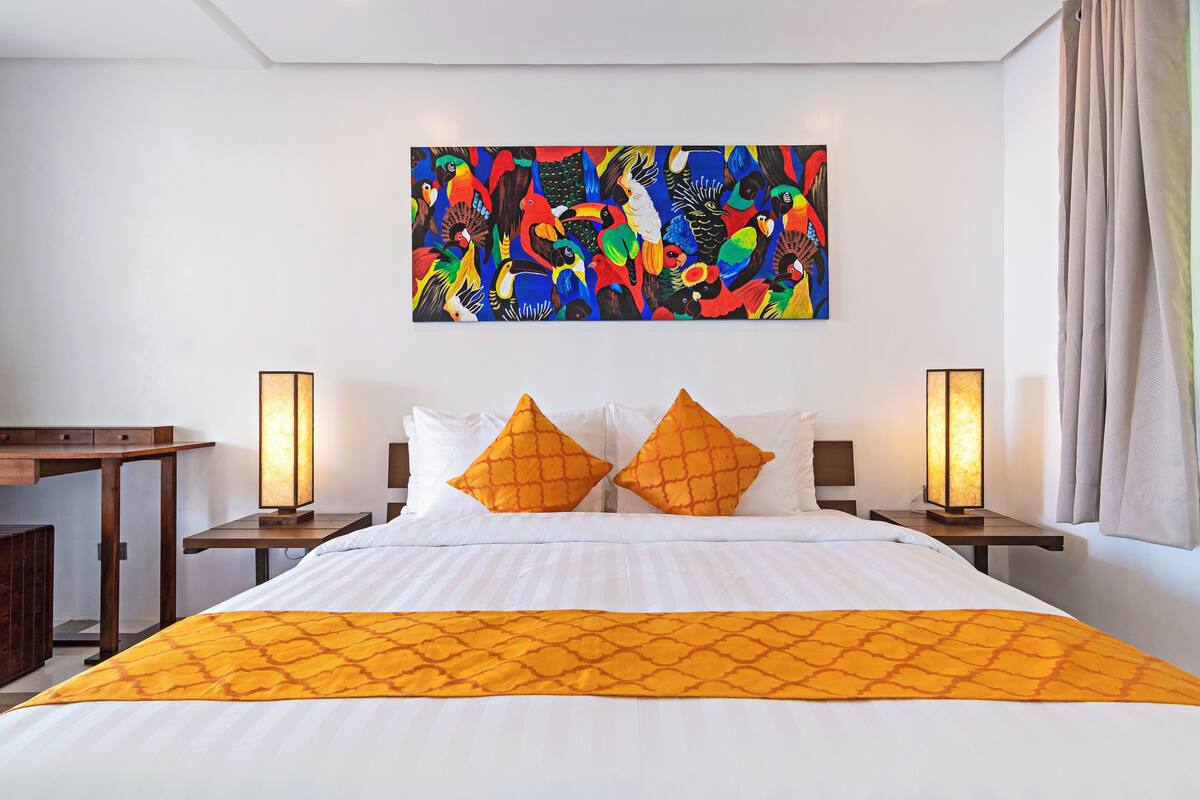 A hotel room with a large bed, two nightstands, a desk, and a colorful abstract painting on the wall.