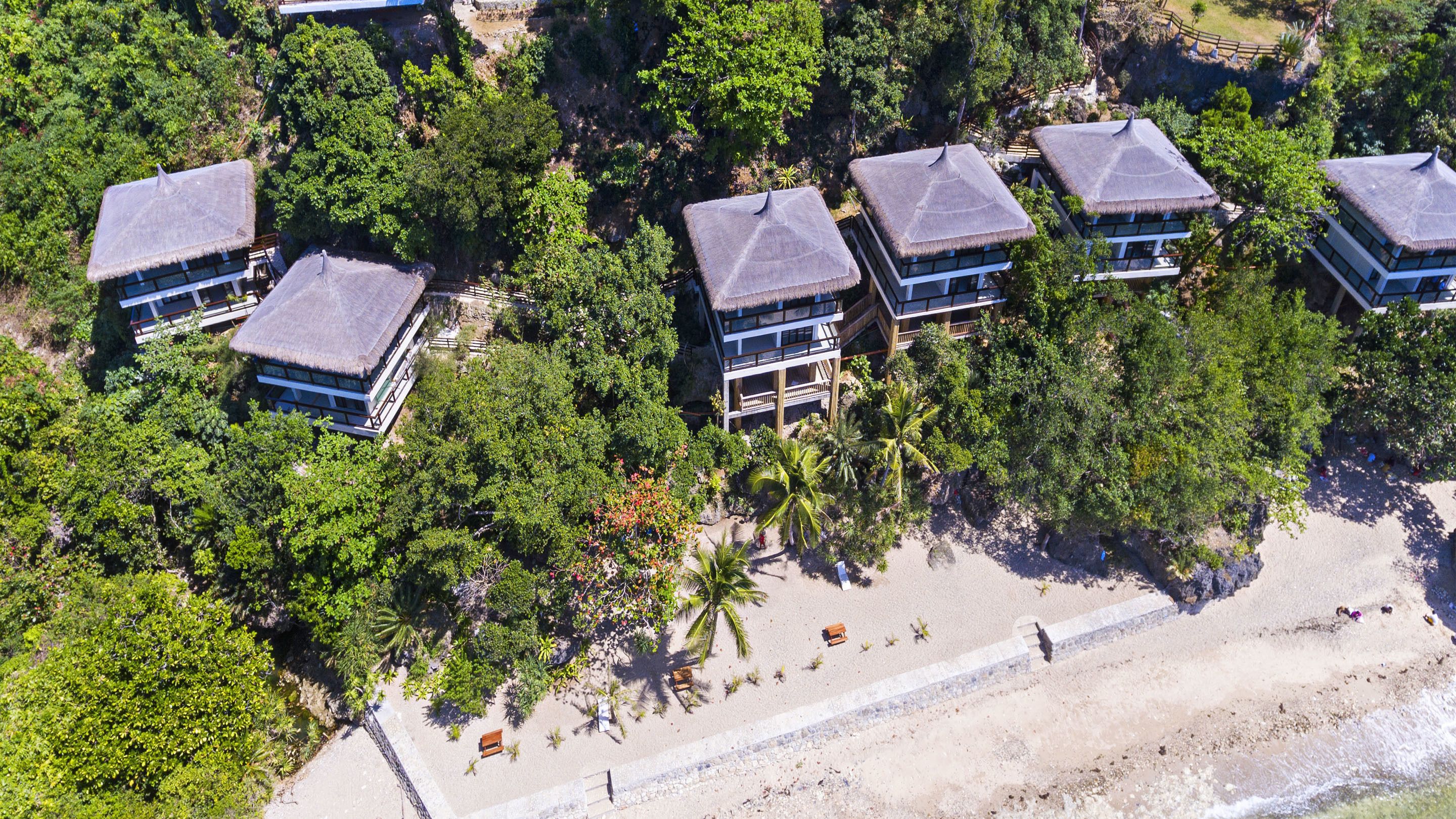 Un resort con varias construcciones rodeado de abundante vegetación y una playa de arena.