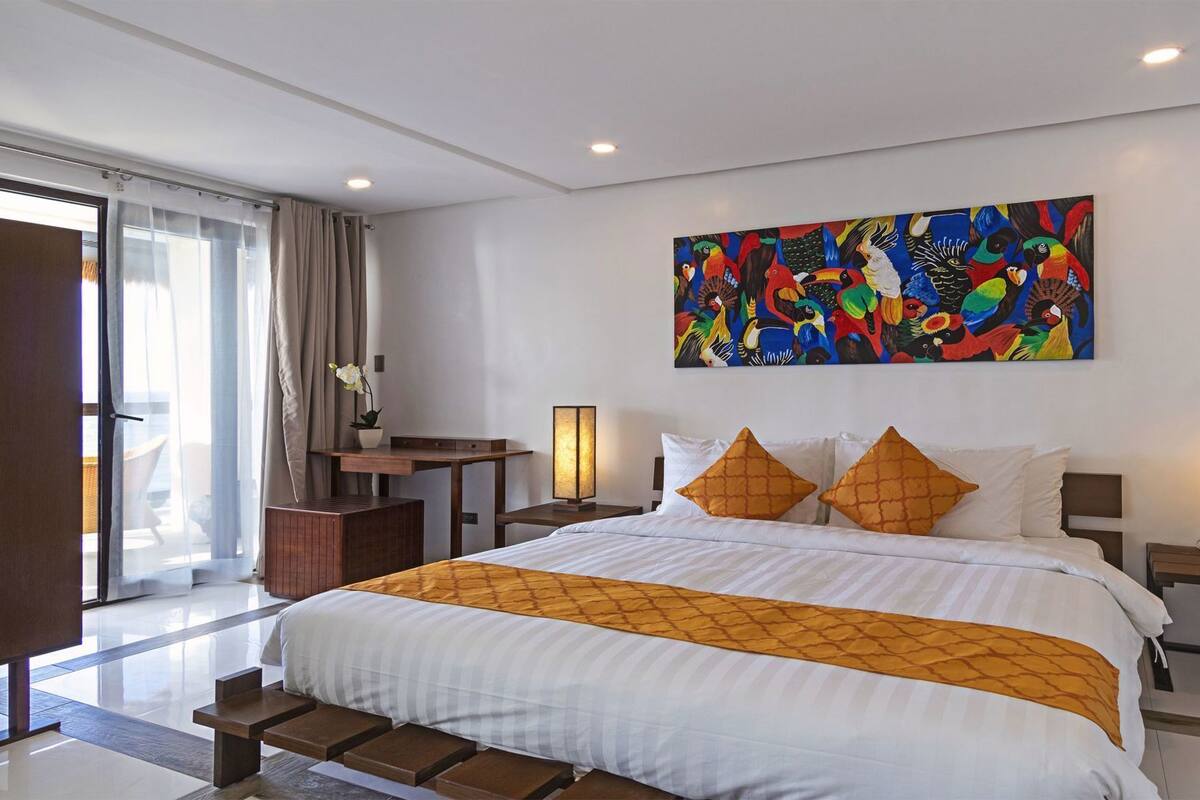 A hotel room with a large bed, a desk, a chair, a lamp, and a painting on the wall.
