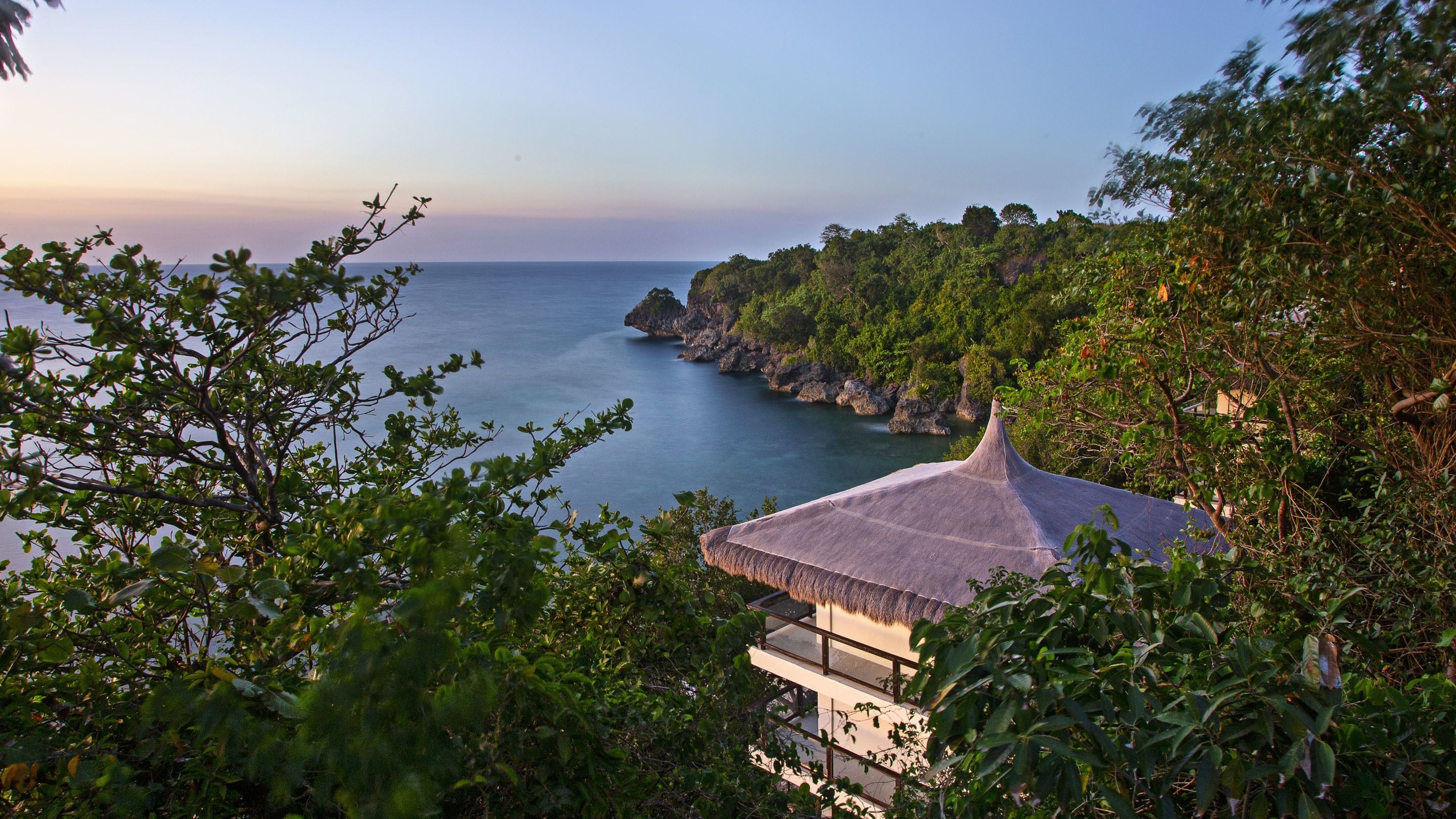 A coastal view with a house overlooking the sea, surrounded by lush greenery.