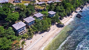 Une propriété située en bord de mer, comprenant plusieurs villas aux toits de chaume, une plage de sable et une eau cristalline.