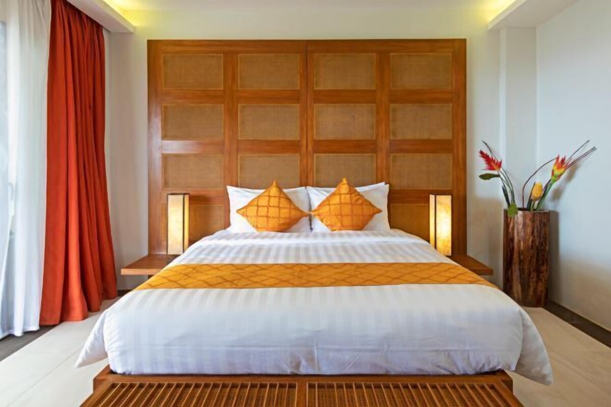 A hotel room with a large bed, wooden headboard, and a nightstand with a lamp.