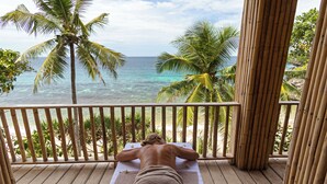 Une personne allongée sur une table de massage, sur une terrasse en bois, avec vue sur l’océan et les palmiers.