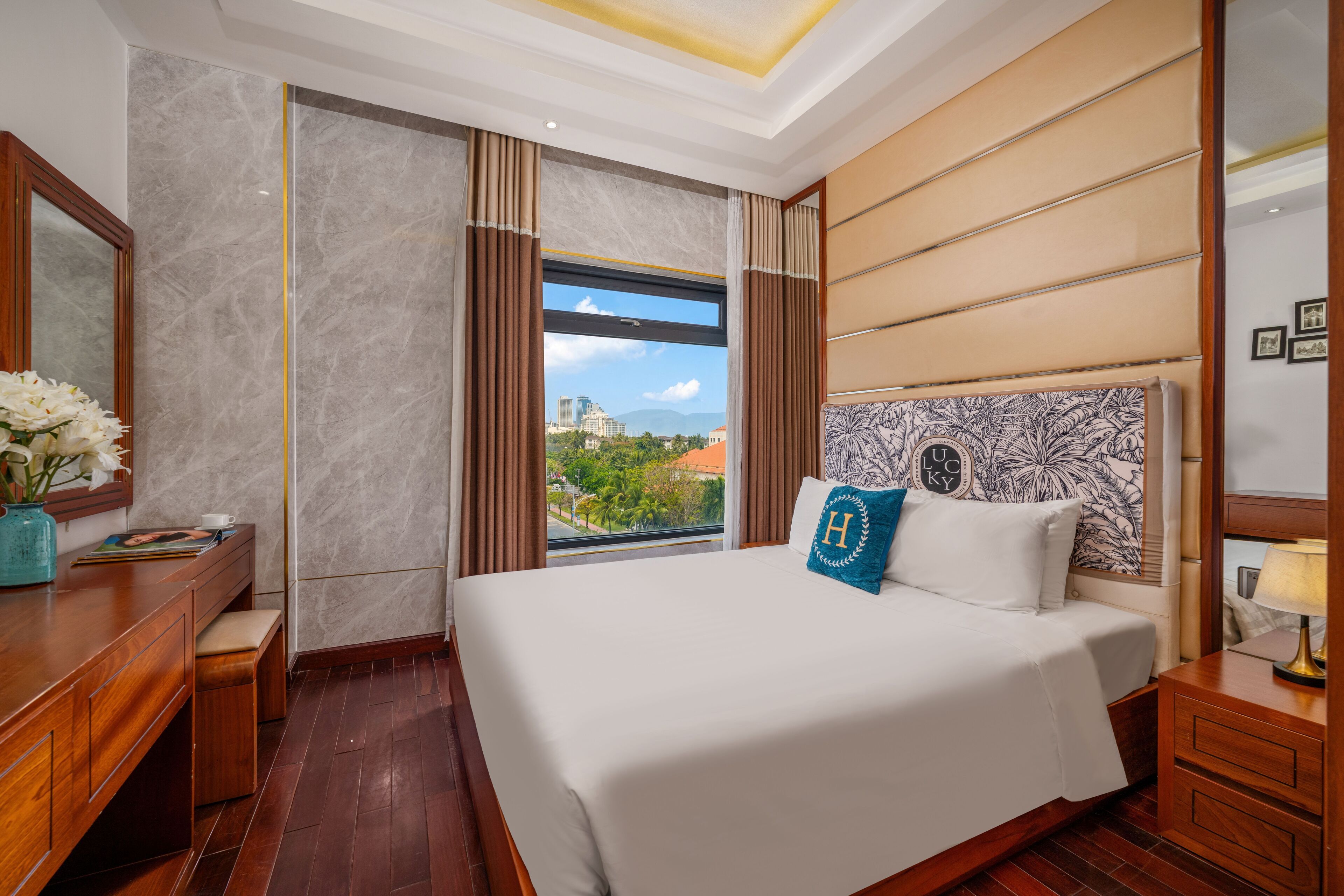 A hotel room with a large bed, a wooden desk, a mirror, and a window with a city view.