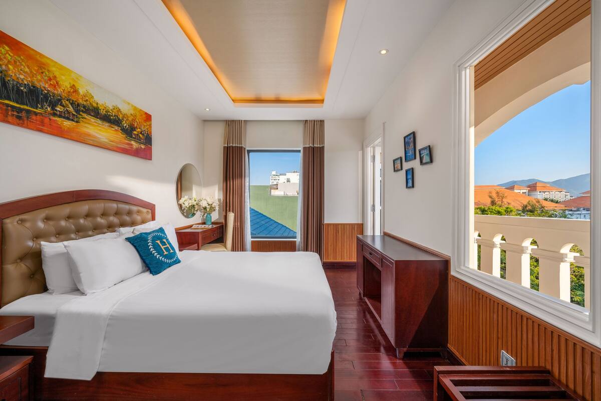 A hotel room with a large bed, a view of the city, and a balcony with a railing.