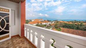 A balcony with a view of a coastal town, a door with decorative glass panels, and a patterned floor.