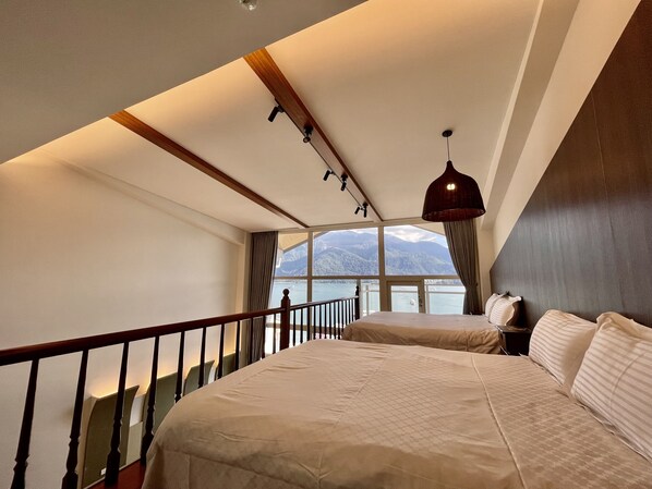 A bedroom with a large bed, a view of mountains, and a balcony with a railing.