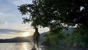 A person standing on a paddleboard near a calm body of water with mountains in the background. - Ming Hu B&B (No elevator) (Yuchi)