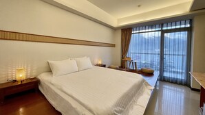A modern hotel room with a large bed, a nightstand, a small table with a lamp, and a view of the outdoors through a large window. - Ming Hu B&B (No elevator) (Yuchi)