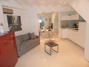 A modern living room with a sofa, a dining table with chairs, and a kitchen area with a sink and cabinets.