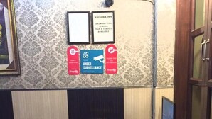 A reception desk with a check-out time sign, surveillance notice, and a framed picture on the wall. - Krishna Inn (New Delhi)