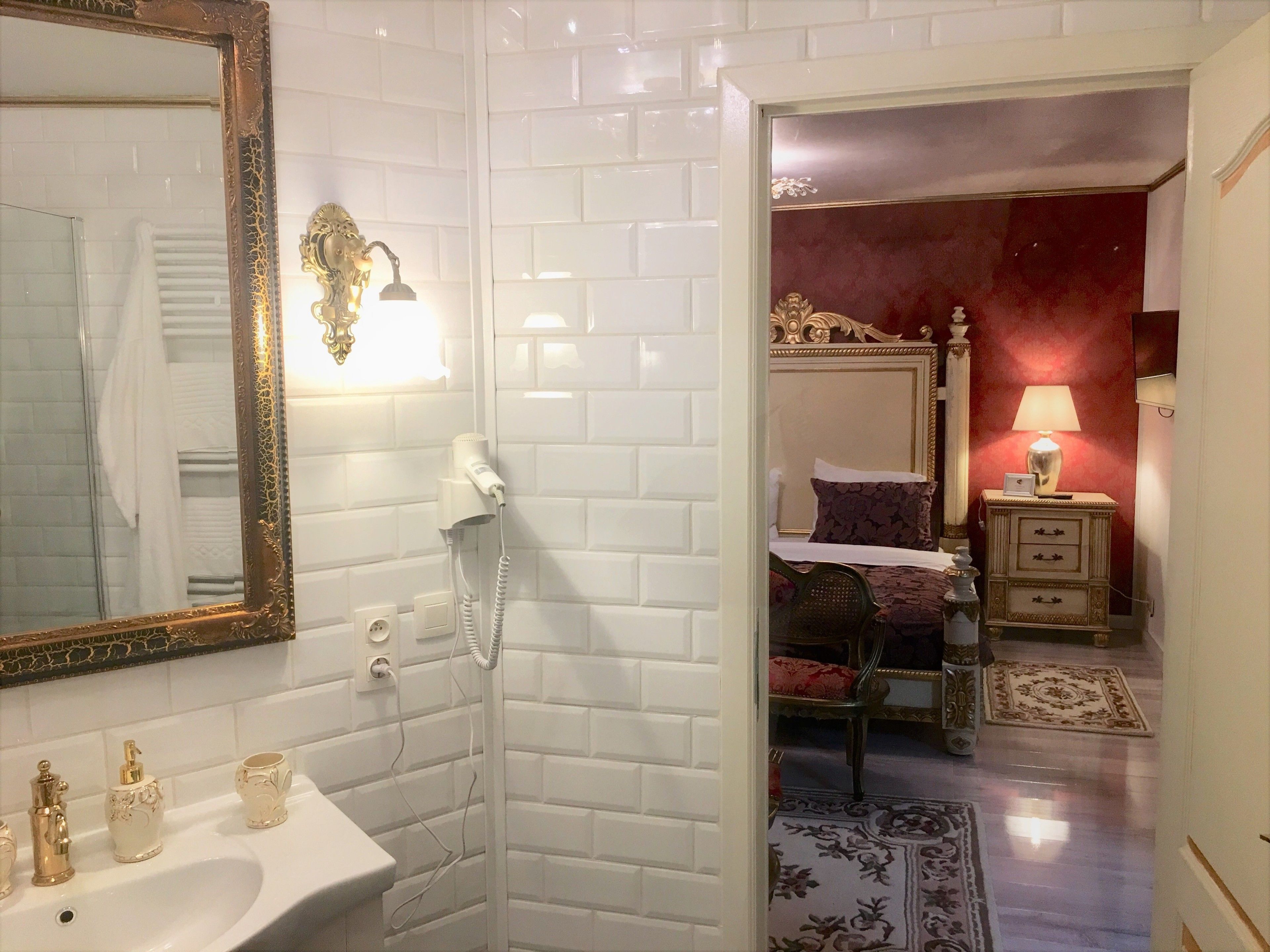 A bathroom with a white sink, a mirror with an ornate frame, and a hairdryer on the wall.