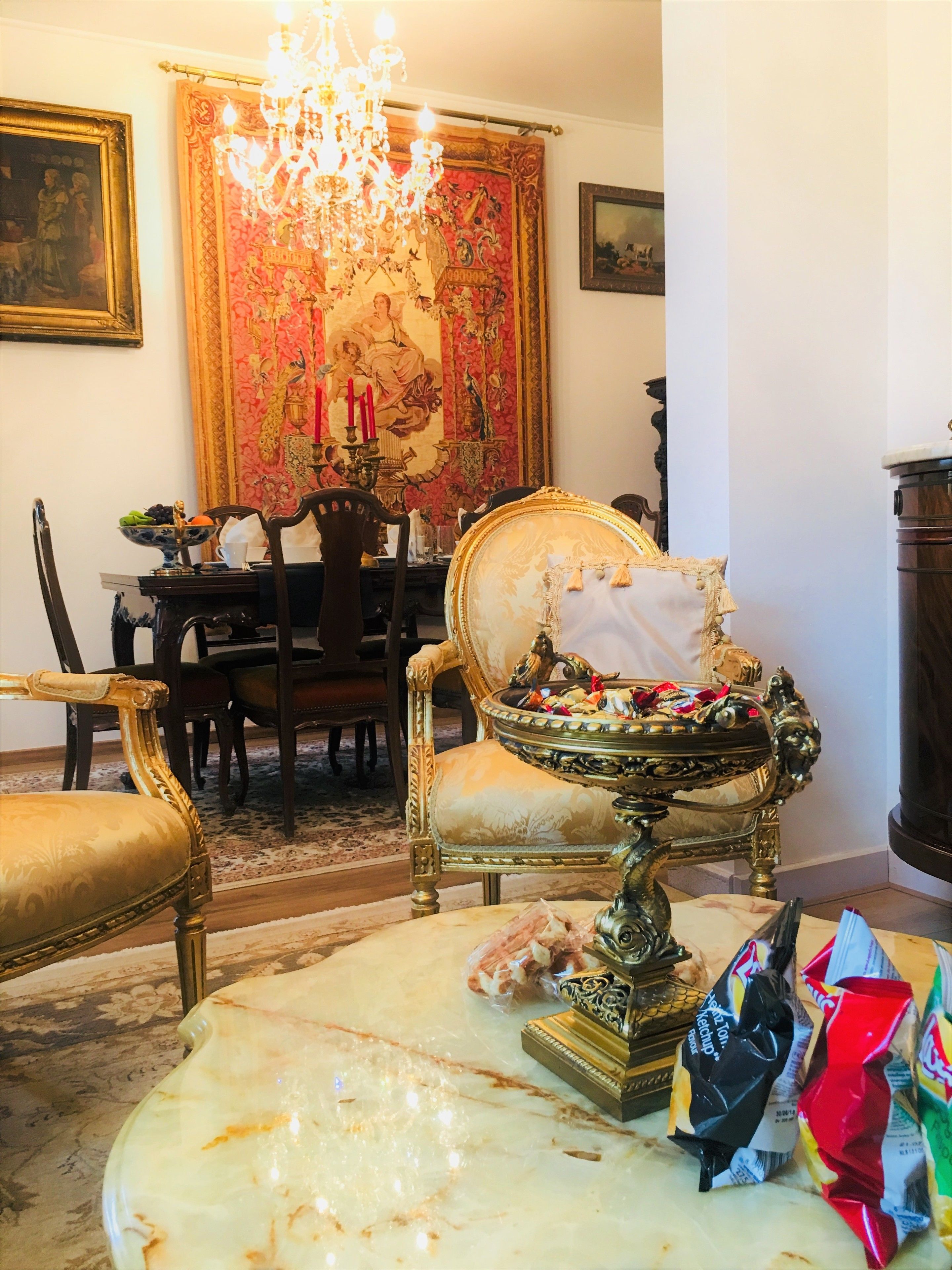 A room with a chandelier, ornate furniture, and a large tapestry.