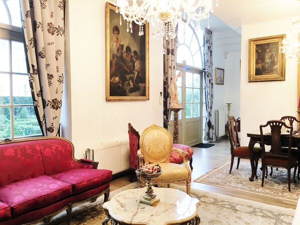 A room with a red sofa, a gold chair, a marble table, and a chandelier. - Koetshuis Bosdam B&B (Beveren)