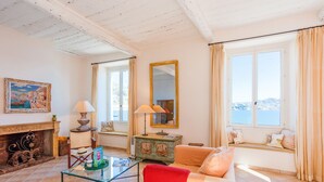 Un salón luminoso con chimenea, un sofá, una mesa de centro de vidrio y vistas al mar a través de amplias ventanas.