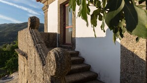 En stenskulptur som föreställer en sittande person, placerad vid ingången till en byggnad med en röd dörr, med utsikt över det omgivande landskapet.