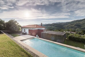 A swimming pool with a view of a house and hills in the background.